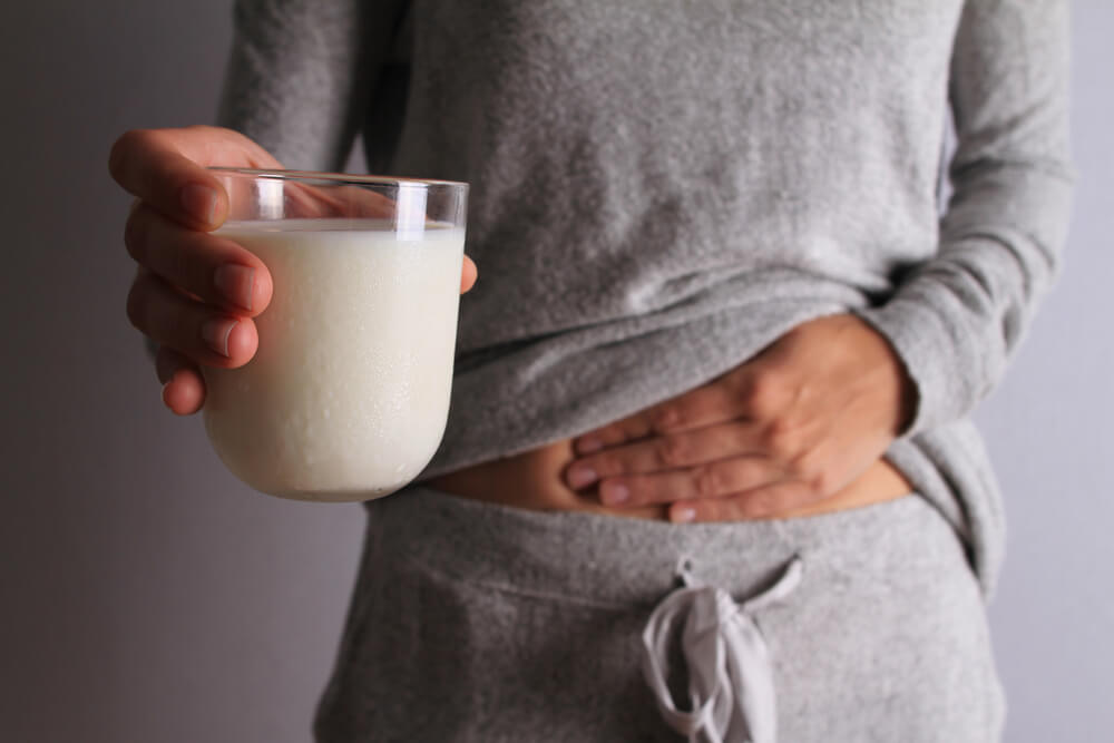 mulher com dor na barriga segurando copo de leite devido a intolerância a lactose