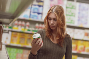 Jovem fazendo compras no supermercado, ela está segurando uma lata e verificando informações no rótulo do produto